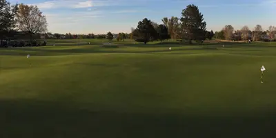 A wide shot of a golf course with trees in the background, against a blue sky.