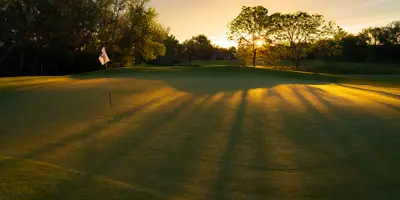 A golf course with a setting sun and trees in the background.