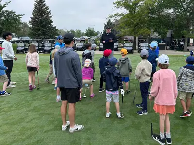 A group of children listen as an adult gives instruction at the golf course.