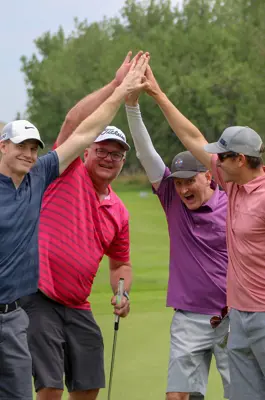Four men high five on a golf course.