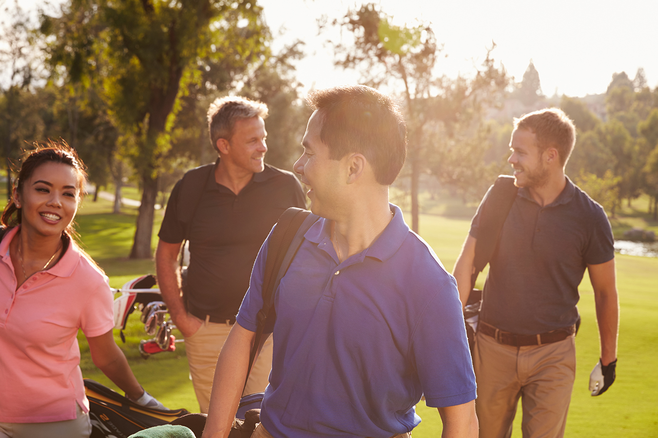 Four adults carrying golf equipment in late afternoon sun.