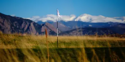 A flag marking a hole on a golf course, with mountains in the background.