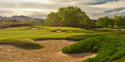 A golf course with a sand trap in the foreground and trees in the background.
