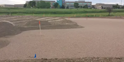 A field with grass in the background and stakes marking out ongoing work.