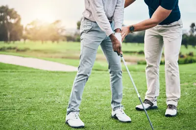 A person holding a golf club and having their position adjusted by another person.